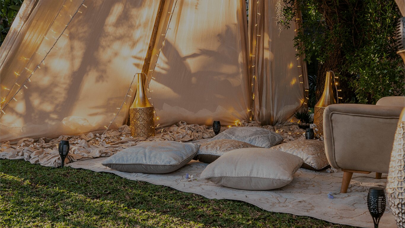 Candlelit tent draped with fairy lights and floor cushions at dusk